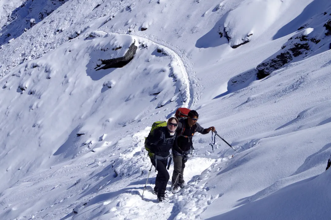 Zwei Wanderer steigen einen steilen, schneebedeckten Berghang im Himalaya hinauf.